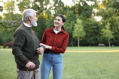 Photo of Smiling caregiver supporting elderly man who using walking cane outdoors. Space for text