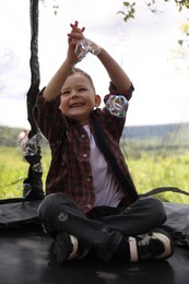 Photo of Happy boy playing with soap bubbles on trampoline outdoors