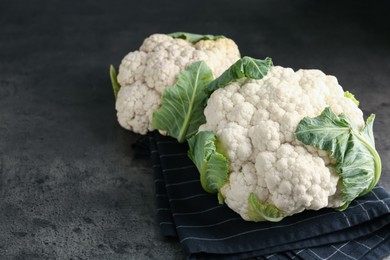 Photo of Fresh cauliflower heads with green leaves on grey table, closeup. Space for text