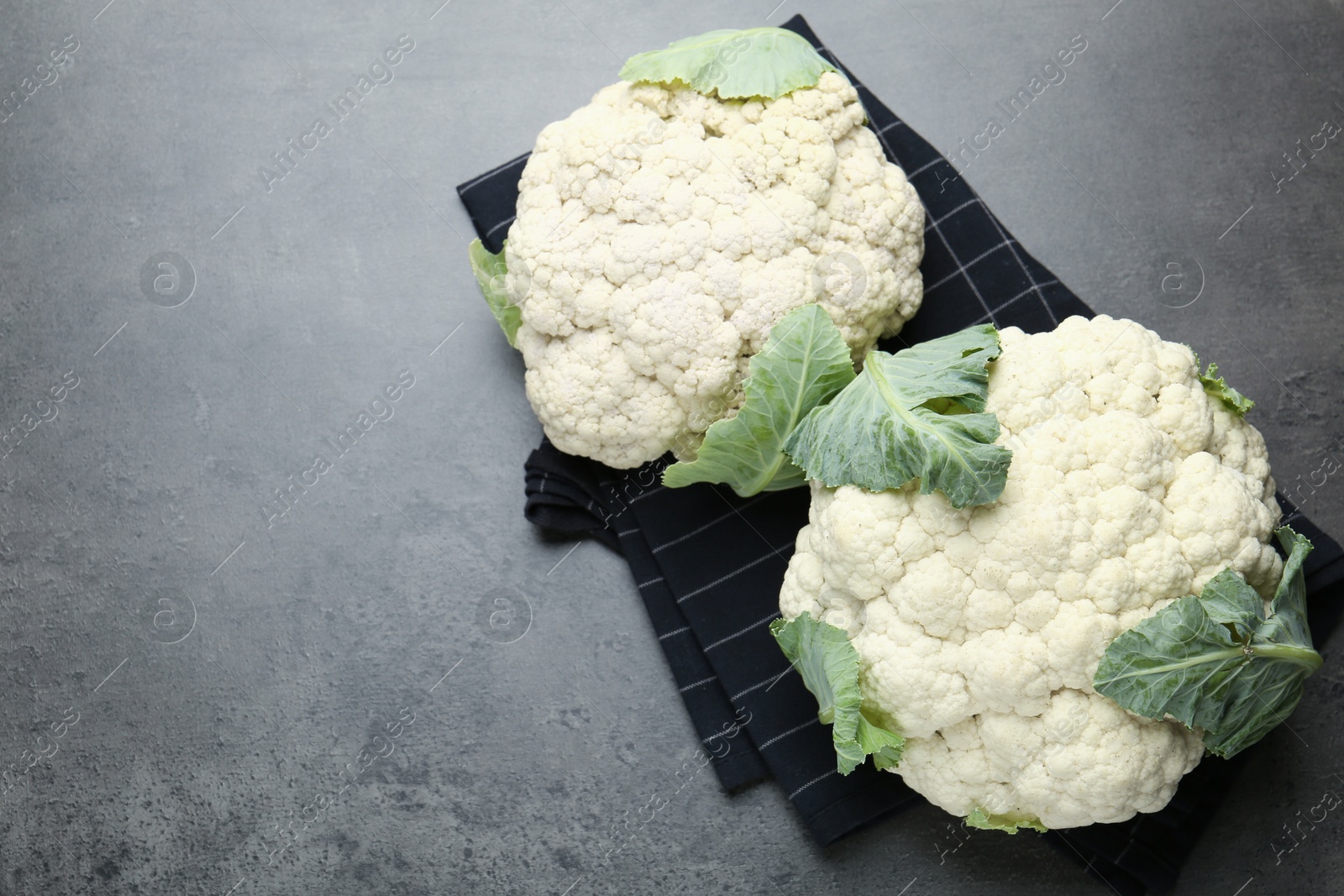 Fresh cauliflower heads with green leaves on grey table, flat lay. Space for text Photo of Fresh cauliflower heads with green leaves on grey table, flat lay. Space for text
