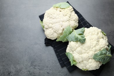 Photo of Fresh cauliflower heads with green leaves on grey table, flat lay. Space for text