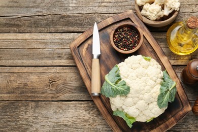 Photo of Fresh cauliflower with green leaves, spices and knife on wooden table, flat lay. Space for text