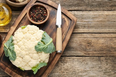 Photo of Fresh cauliflower with green leaves, spices and knife on wooden table, flat lay. Space for text