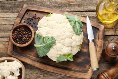 Photo of Fresh cauliflower with green leaves, spices and knife on wooden table, flat lay