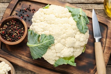 Photo of Fresh cauliflower with green leaves, spices and knife on wooden table, flat lay