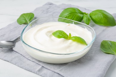 Photo of Tasty yoghurt with basil in bowl on white table, closeup