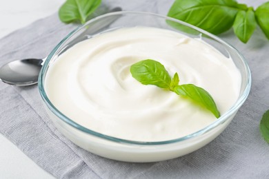 Photo of Tasty yoghurt with basil in bowl on white table, closeup