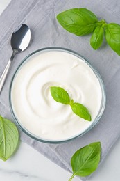 Photo of Tasty yoghurt with basil in bowl on white table, flat lay