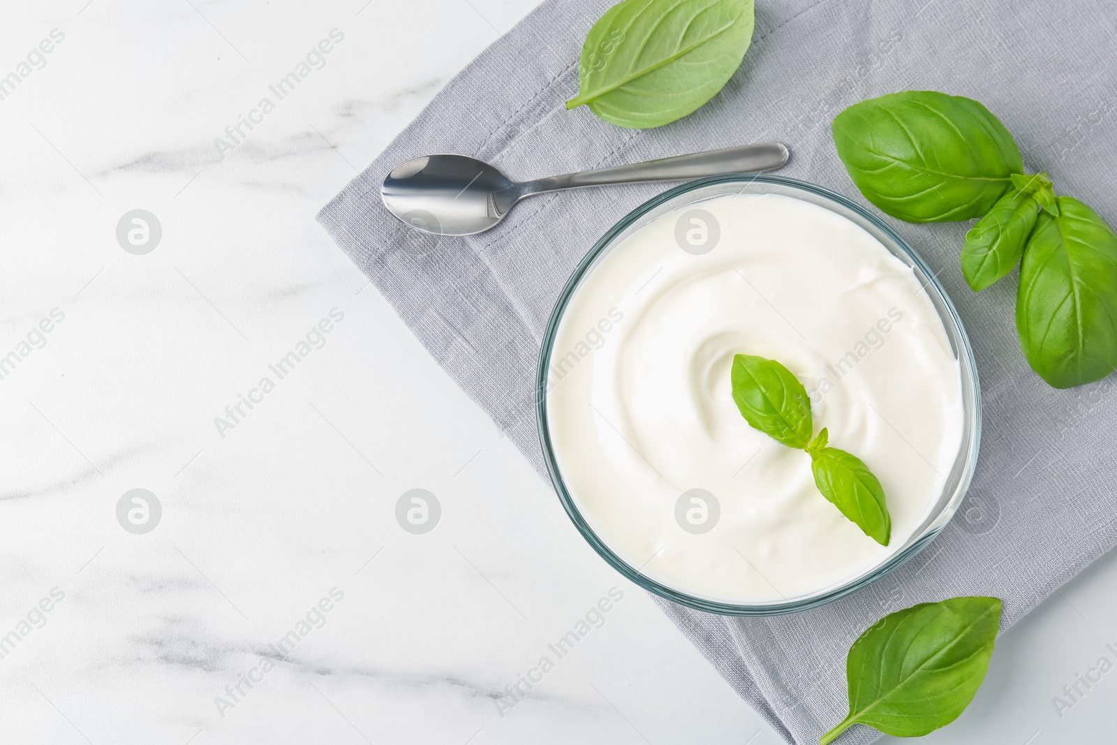 Photo of Tasty yoghurt with basil in bowl on white marble table, flat lay. Space for text