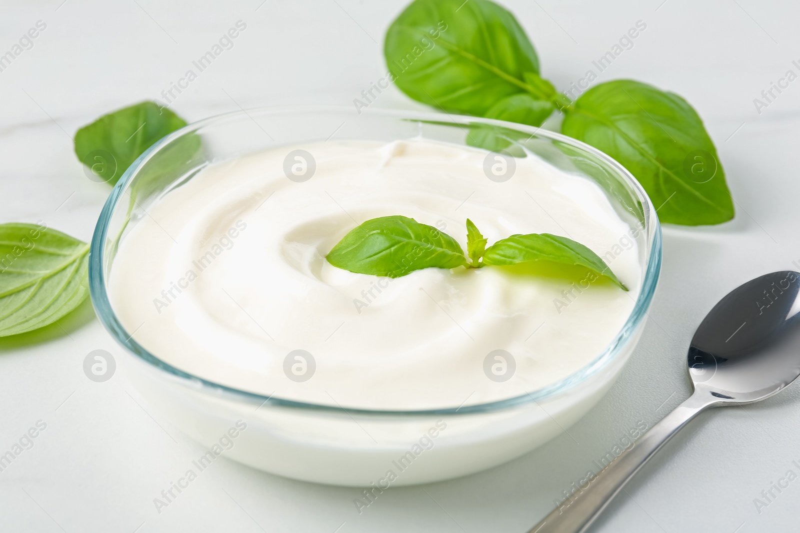 Tasty yoghurt with basil in bowl on white table, closeup Photo of Tasty yoghurt with basil in bowl on white table, closeup