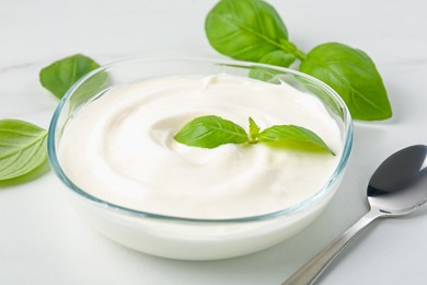 Photo of Tasty yoghurt with basil in bowl on white table, closeup