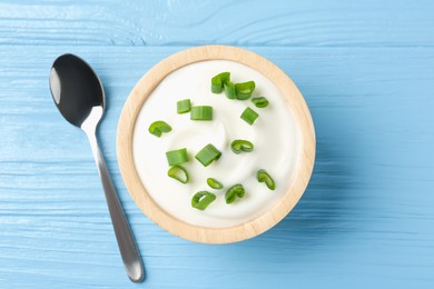 Photo of Tasty yoghurt with green onions in bowl on light blue wooden table, top view