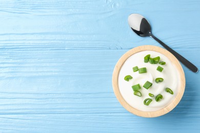 Photo of Tasty yoghurt with green onions in bowl on light blue wooden table, top view. Space for text