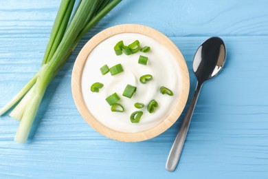 Photo of Tasty yoghurt with green onions in bowl on light blue wooden table, flat lay