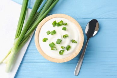 Photo of Tasty yoghurt with green onions in bowl on light blue wooden table, flat lay