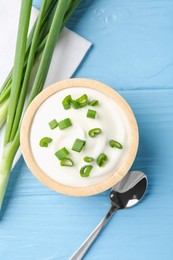 Photo of Tasty yoghurt with green onions in bowl on light blue wooden table, flat lay