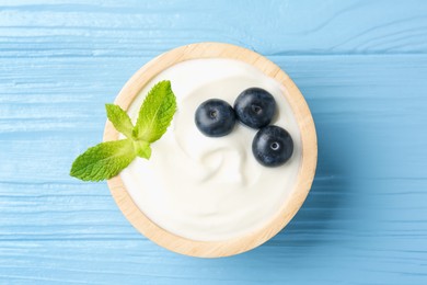 Photo of Tasty yoghurt with blueberries and mint in bowl on light blue wooden table, top view