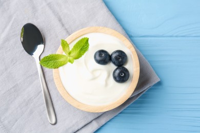 Photo of Tasty yoghurt with blueberries and mint in bowl on light blue wooden table, top view