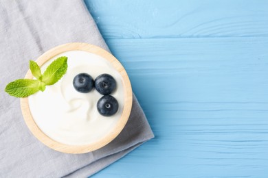 Photo of Tasty yoghurt with blueberries and mint in bowl on light blue wooden table, top view. Space for text