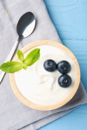 Photo of Tasty yoghurt with blueberries and mint in bowl on light blue wooden table, top view