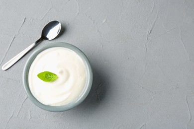 Photo of Tasty yoghurt with basil in bowl on light grey table, top view. Space for text