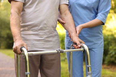 Photo of Nurse helping elderly man who using walking frame outdoors, closeup