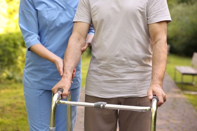 Photo of Nurse helping elderly man who using walking frame outdoors, closeup