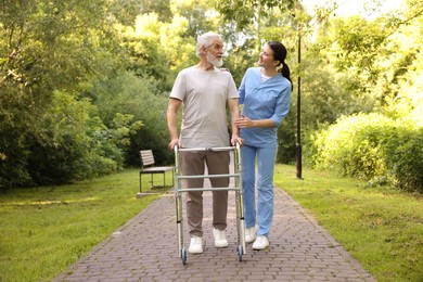 Photo of Smiling nurse supporting elderly man who using walking frame outdoors
