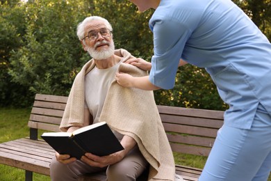 Photo of Nurse supporting smiling elderly man in glasses with book outdoors, closeup