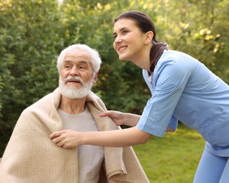 Photo of Smiling nurse with elderly man wrapped in blanket outdoors