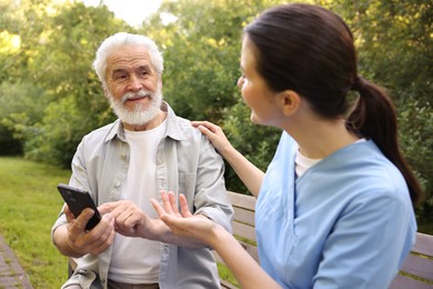 Photo of Nurse and elderly man using smartphone on bench outdoors