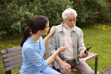 Photo of Nurse and elderly man using smartphone on bench outdoors