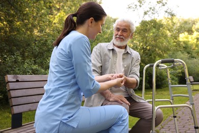 Photo of Nurse supporting elderly man with walking frame on bench outdoors