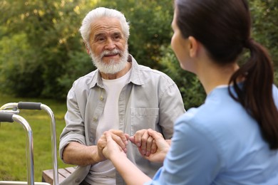 Photo of Nurse supporting elderly man with walking frame outdoors