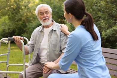 Photo of Nurse supporting elderly man with walking frame on bench outdoors