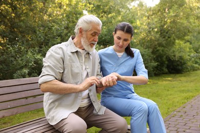 Photo of Nurse supporting elderly man on bench outdoors