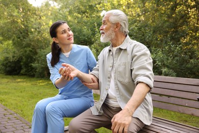 Photo of Nurse supporting elderly man on bench outdoors