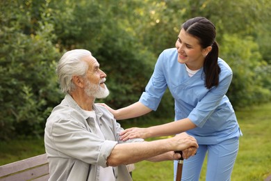 Photo of Smiling nurse supporting elderly man with walking cane outdoors