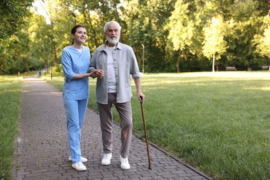 Photo of Smiling nurse supporting elderly man with walking cane outdoors