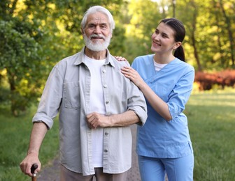 Photo of Smiling nurse supporting elderly man with walking cane outdoors