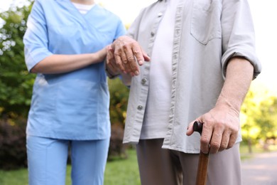 Photo of Nurse supporting elderly man with walking cane outdoors, closeup