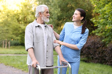 Photo of Smiling nurse supporting elderly man who using walking frame outdoors