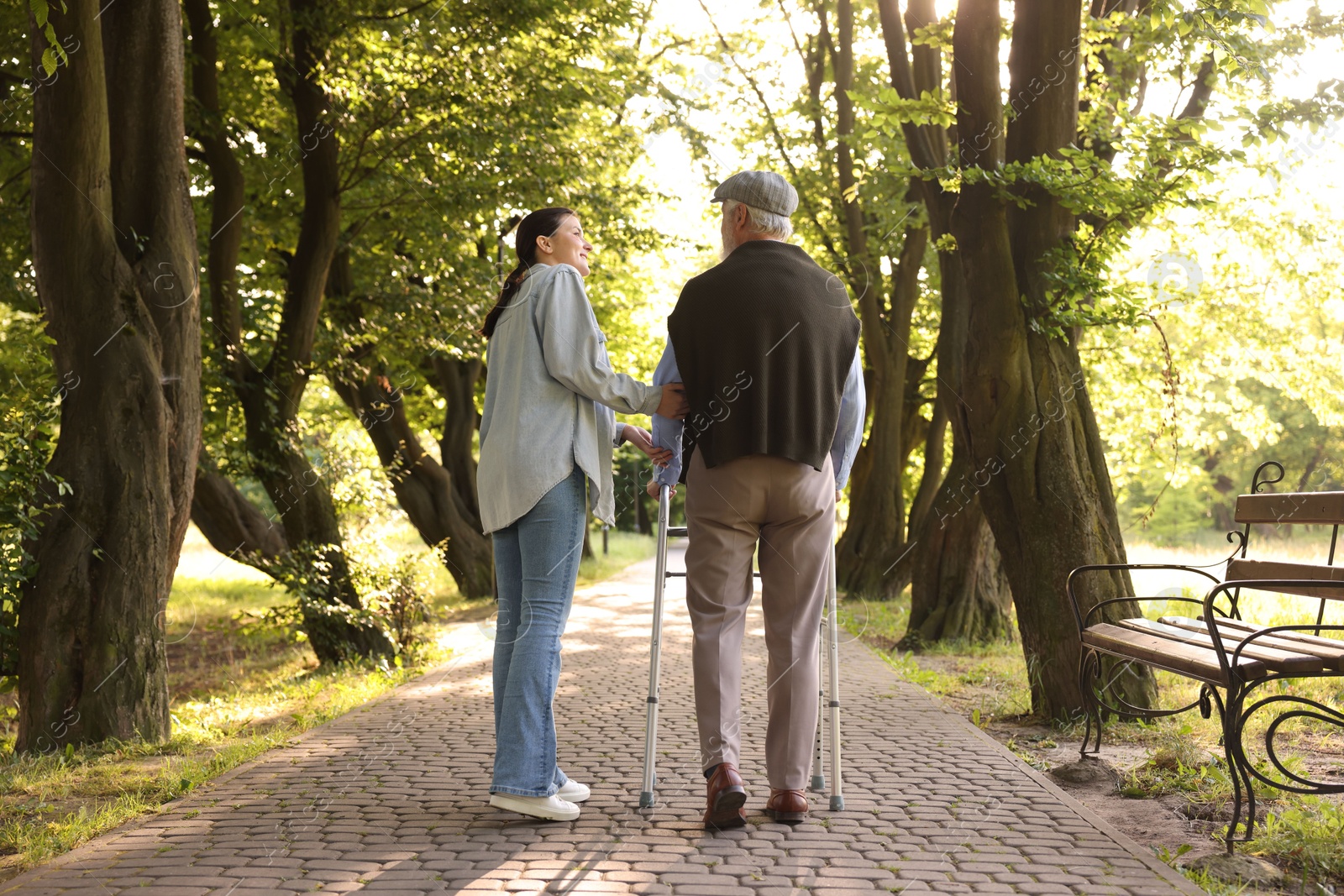 Smiling caregiver supporting elderly man who using walking frame outdoors, back view Photo of Smiling caregiver supporting elderly man who using walking frame outdoors, back view