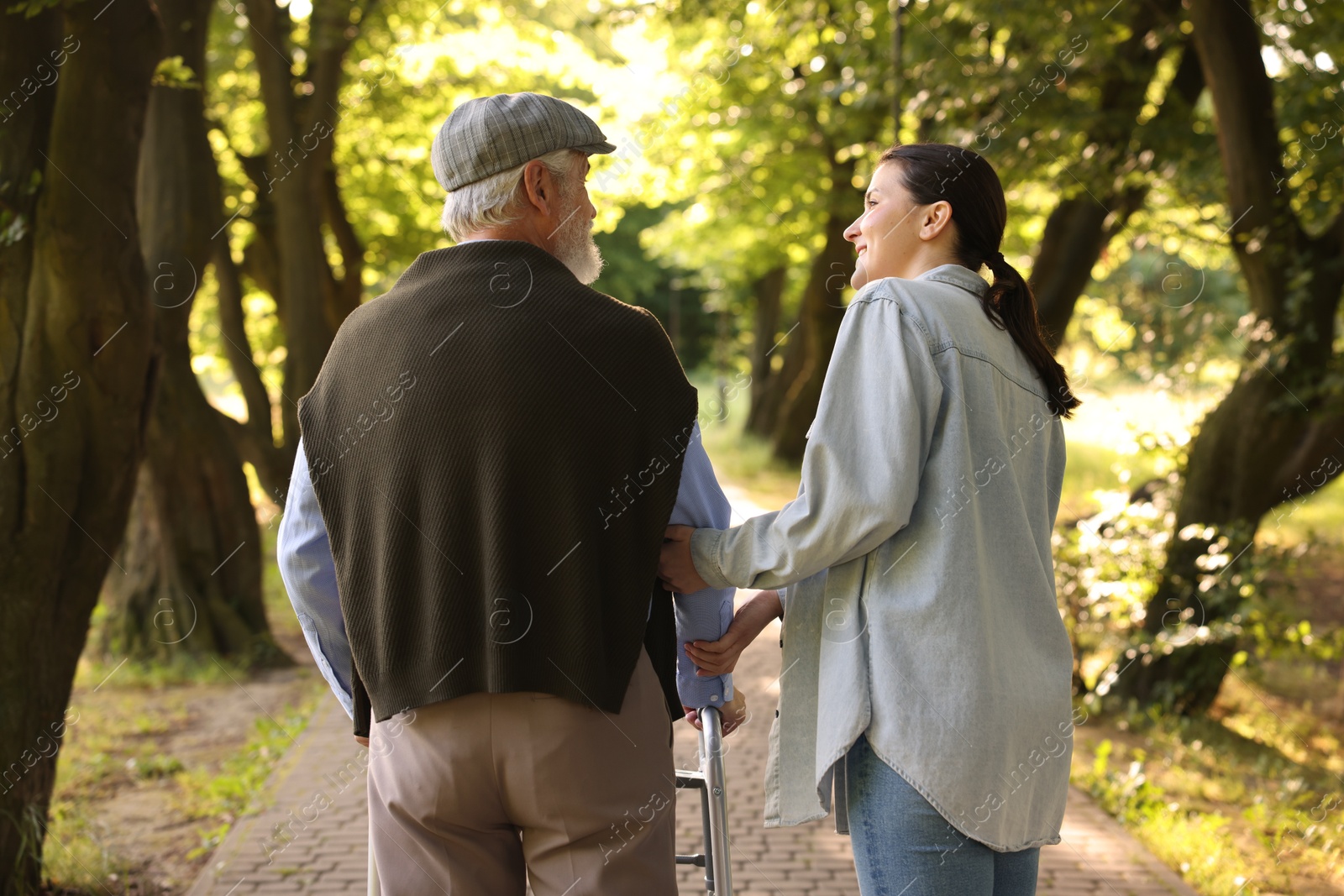 Smiling caregiver supporting elderly man who using walking frame outdoors, back view Photo of Smiling caregiver supporting elderly man who using walking frame outdoors, back view
