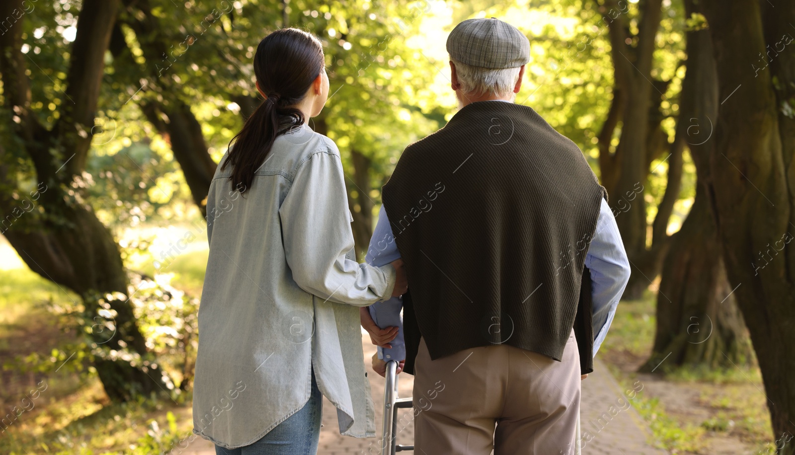 Caregiver supporting elderly man who using walking frame outdoors, back view Photo of Caregiver supporting elderly man who using walking frame outdoors, back view