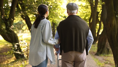 Photo of Caregiver supporting elderly man who using walking frame outdoors, back view