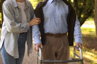 Photo of Caregiver supporting elderly man who using walking frame outdoors, closeup