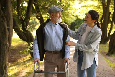 Photo of Smiling caregiver supporting elderly man who using walking frame outdoors
