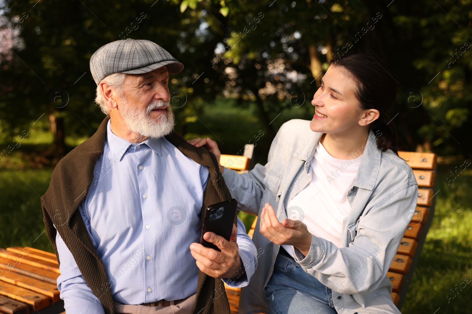 Smiling caregiver and elderly man using smartphone on bench outdoors Photo of Smiling caregiver and elderly man using smartphone on bench outdoors