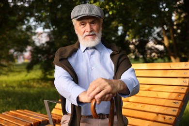 Photo of Handsome elderly man with walking cane sitting on bench outdoors